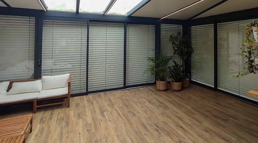 Intérieur moderne avec véranda vitrée, canapé en bois et coussins blancs, plantes vertes en pots