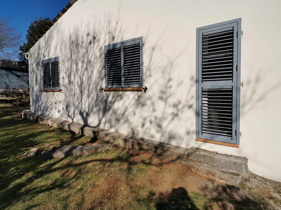 Façade extérieure d'une maison avec trois volets battants gris à persiennes fermés, encadrements en bois naturel