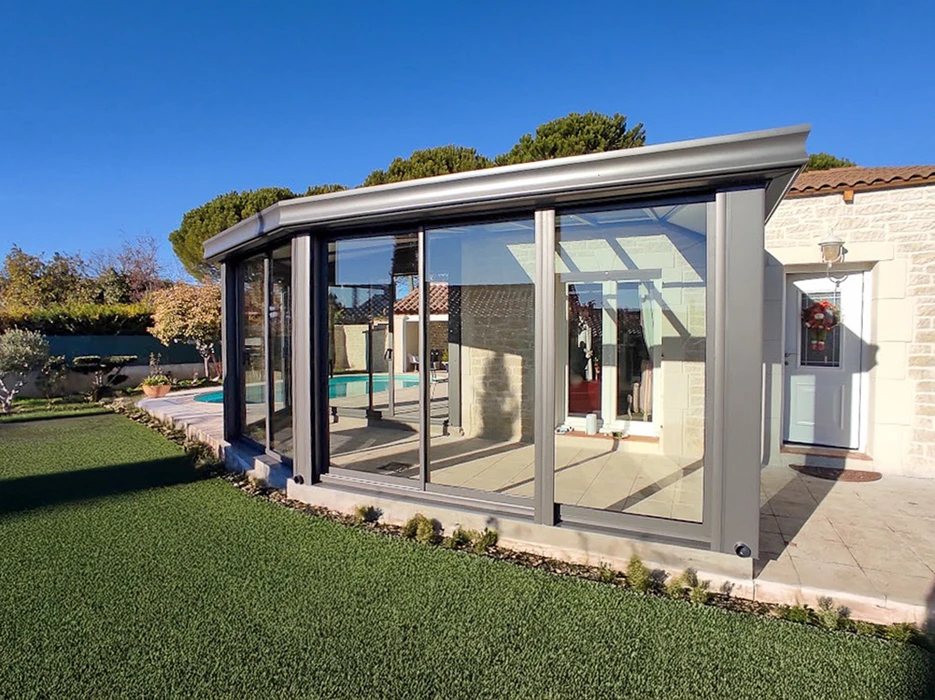 Véranda moderne fermée avec structure en aluminium anthracite, intégrée à maison traditionnelle