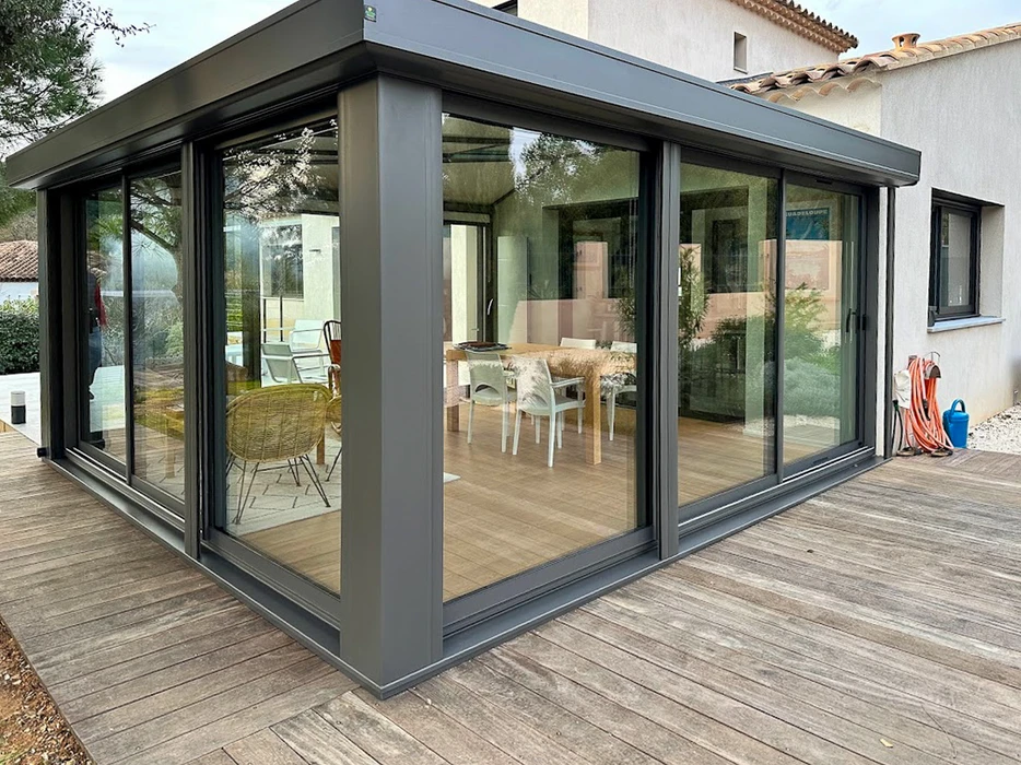 Véranda moderne fermée avec structure en aluminium anthracite, intégrée à maison traditionnelle