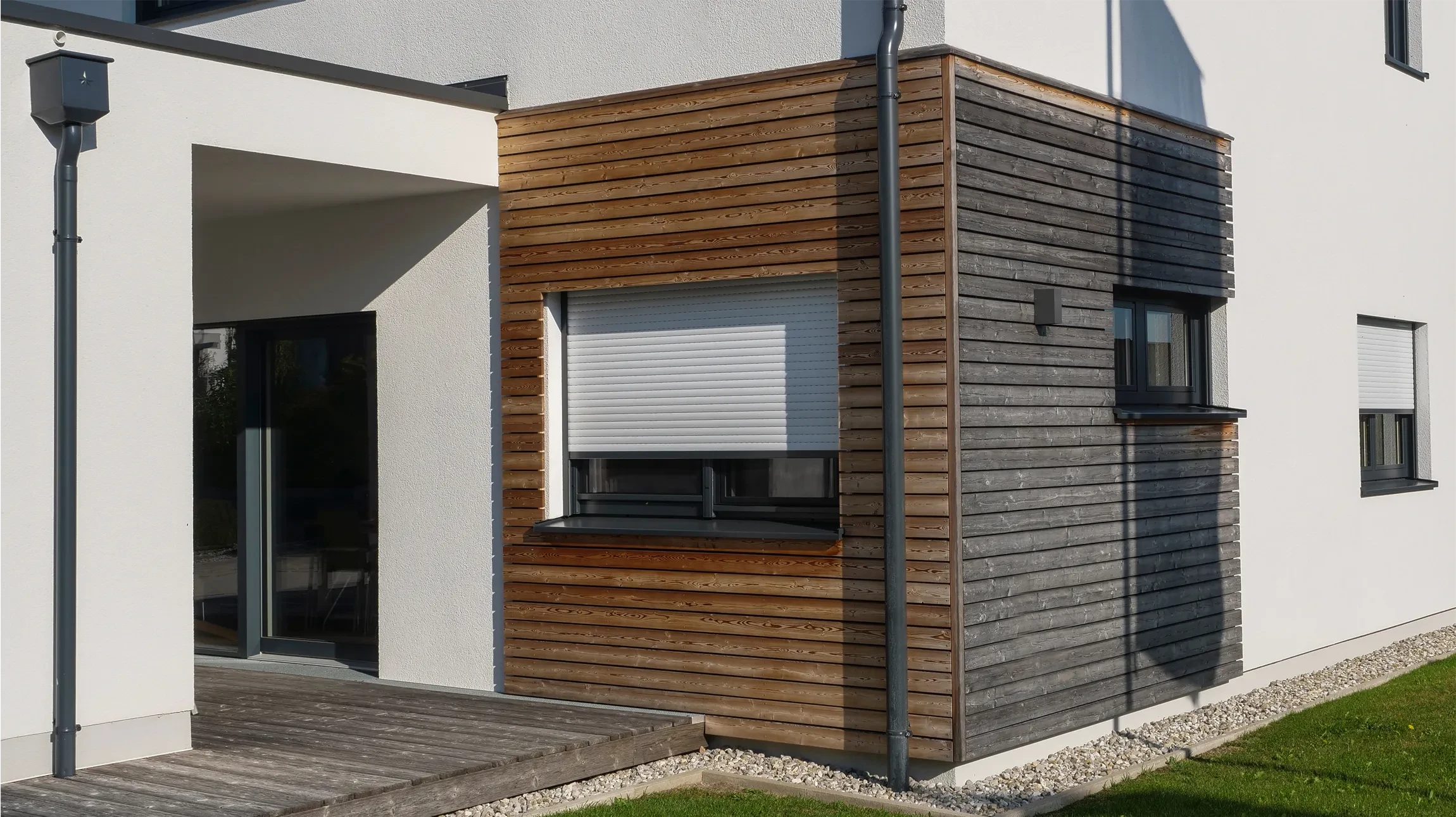 Façade extérieure résidentielle avec volet roulant brun fermé, mur en pierre naturelle et lierre vert