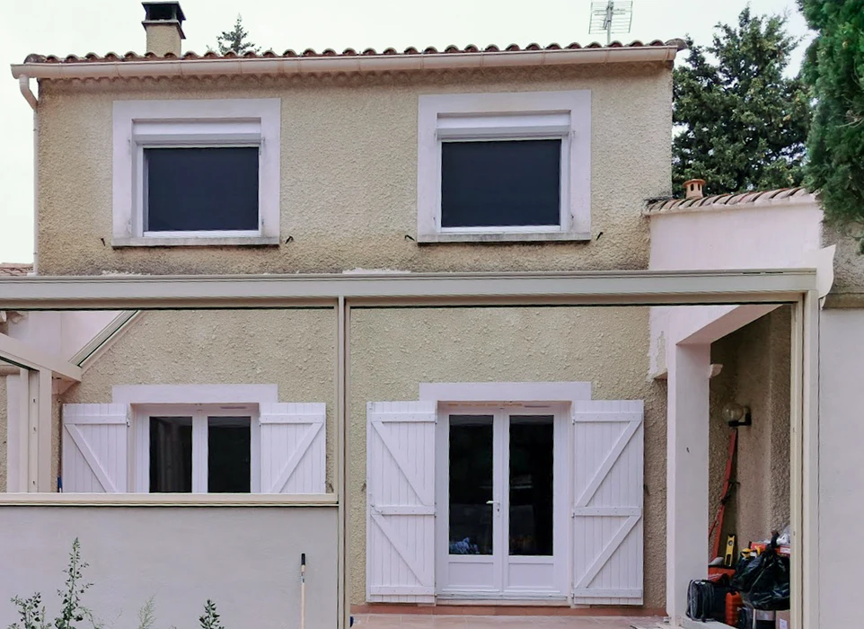 Véranda moderne en construction avec structure métallique noire et grandes baies vitrées panoramiques