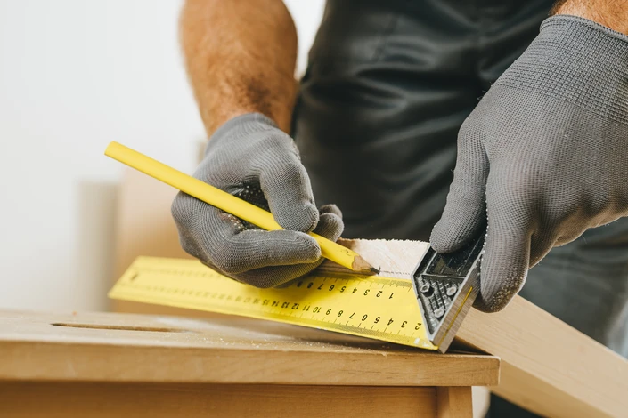 Menuisier en action clouant des planches de bois avec marteau, portant gants de protection blancs